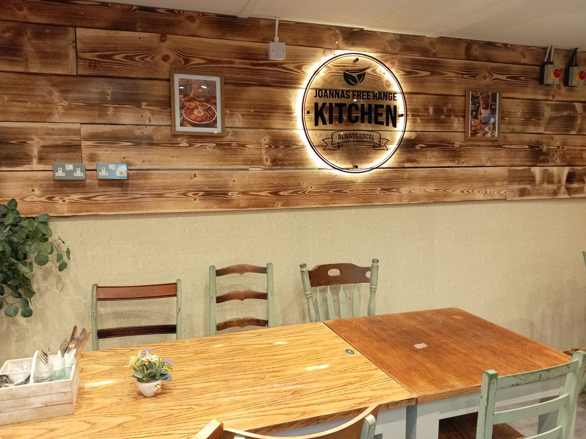 Inside Joanna's Free Range Kitchen, the cafe at Easter Compton Farm Shop, with wooden tables under the lit sign